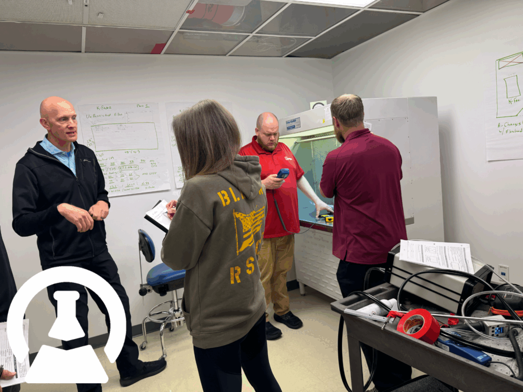 Students taking notes and practicing with certification equipment while instructor teaches from in front of a biosafety cabinet.
