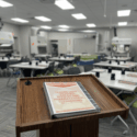 A podium holding a class binder, the title is Testing HEPA Filtered Systems and Pharmaceutical Cleanrooms. The classroom in the background is all set up and ready for the students to arrive.